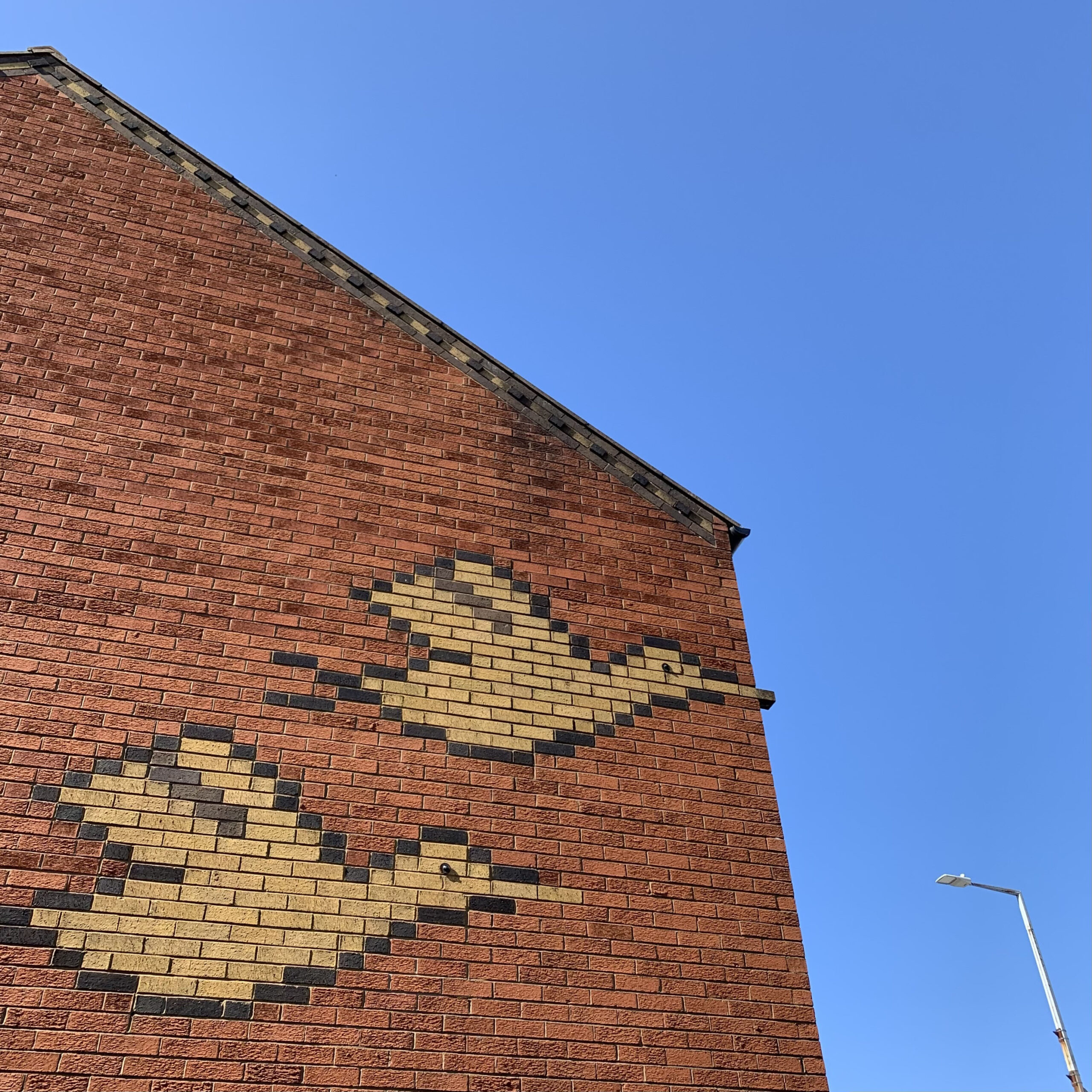 Image of patterned bricks - yellow bricks with black edging make out two flying birds against red bricks on side of building.