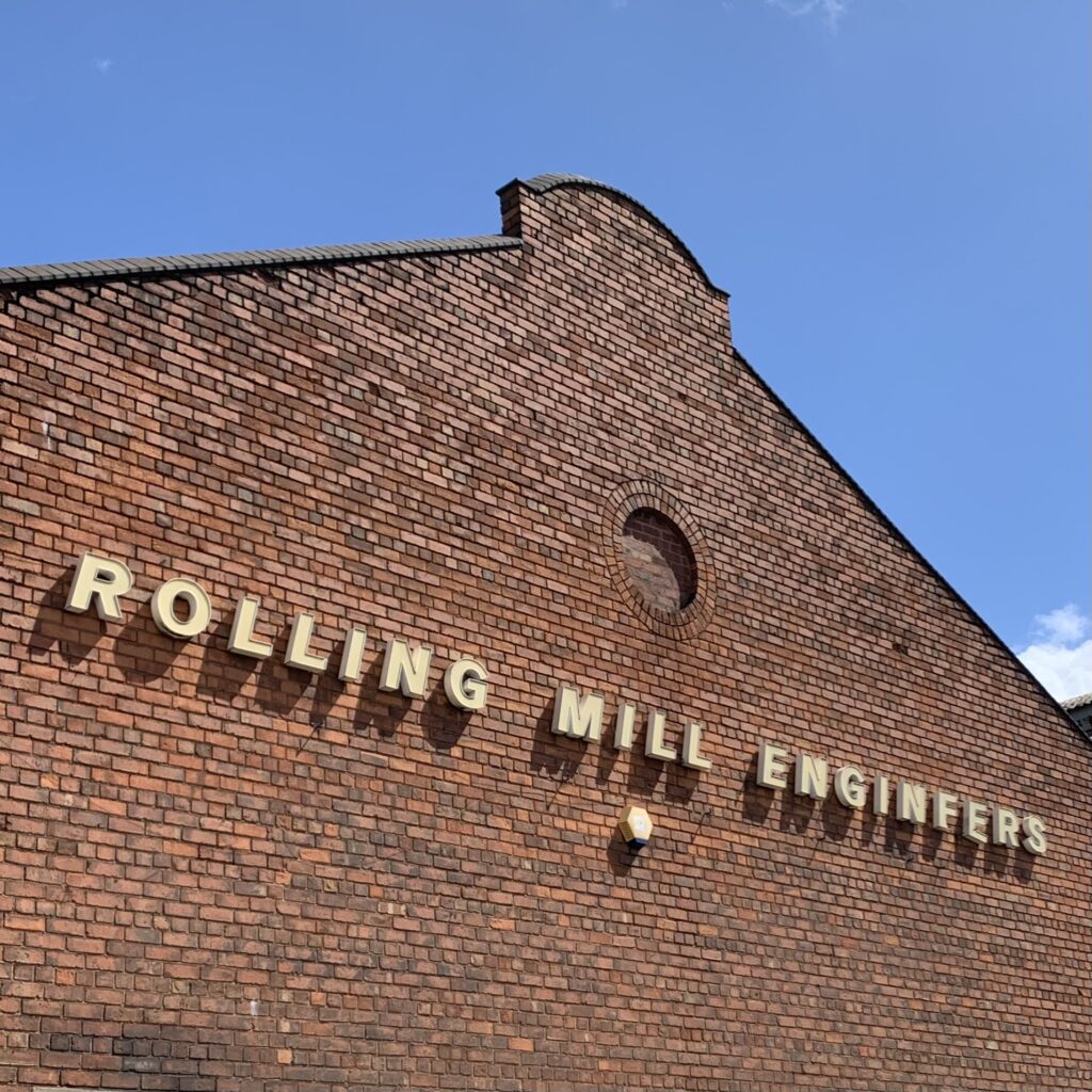Image of side of brick building with 'Rolling Mill Engineers' lettering along the side. Blue sky above.