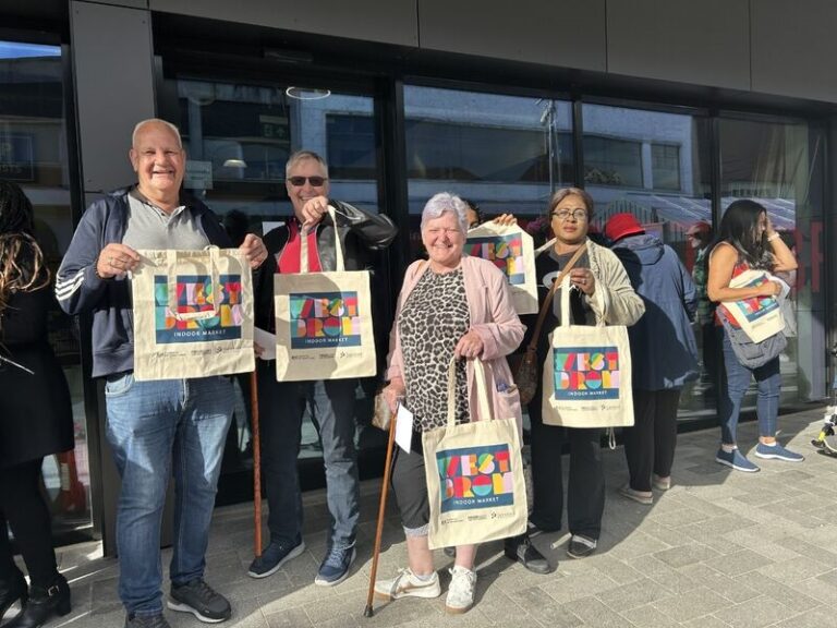 Group of shoppers holding up West Brom market tote bags in a queue waiting for things to open