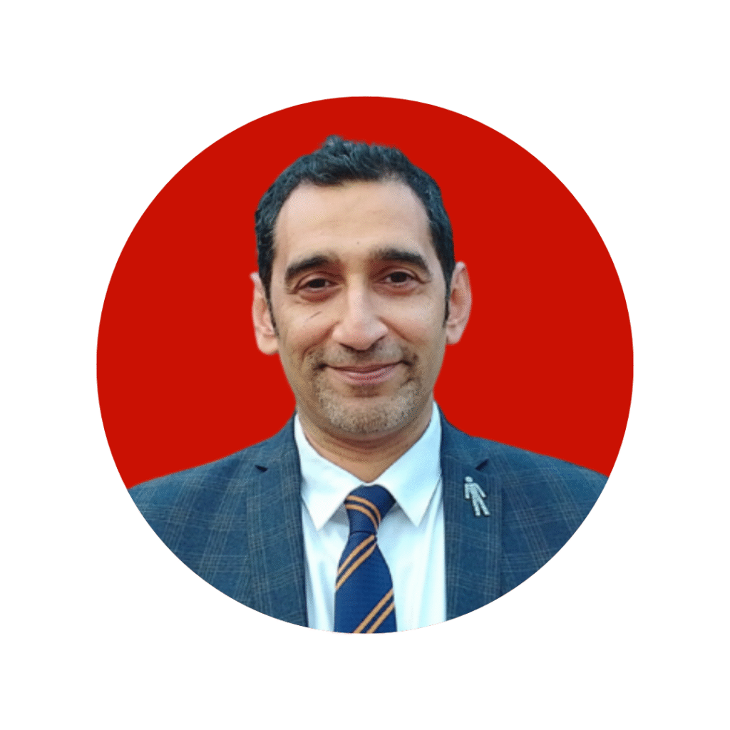 Man with dark hair in shirt, tie and suit smiling at camera.