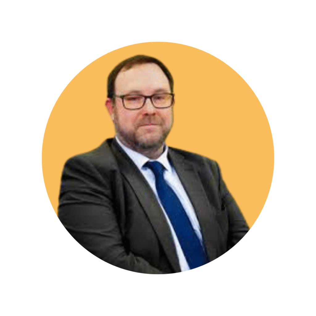Man with dark hair, glasses and beard in suit, shirt and tie smiling