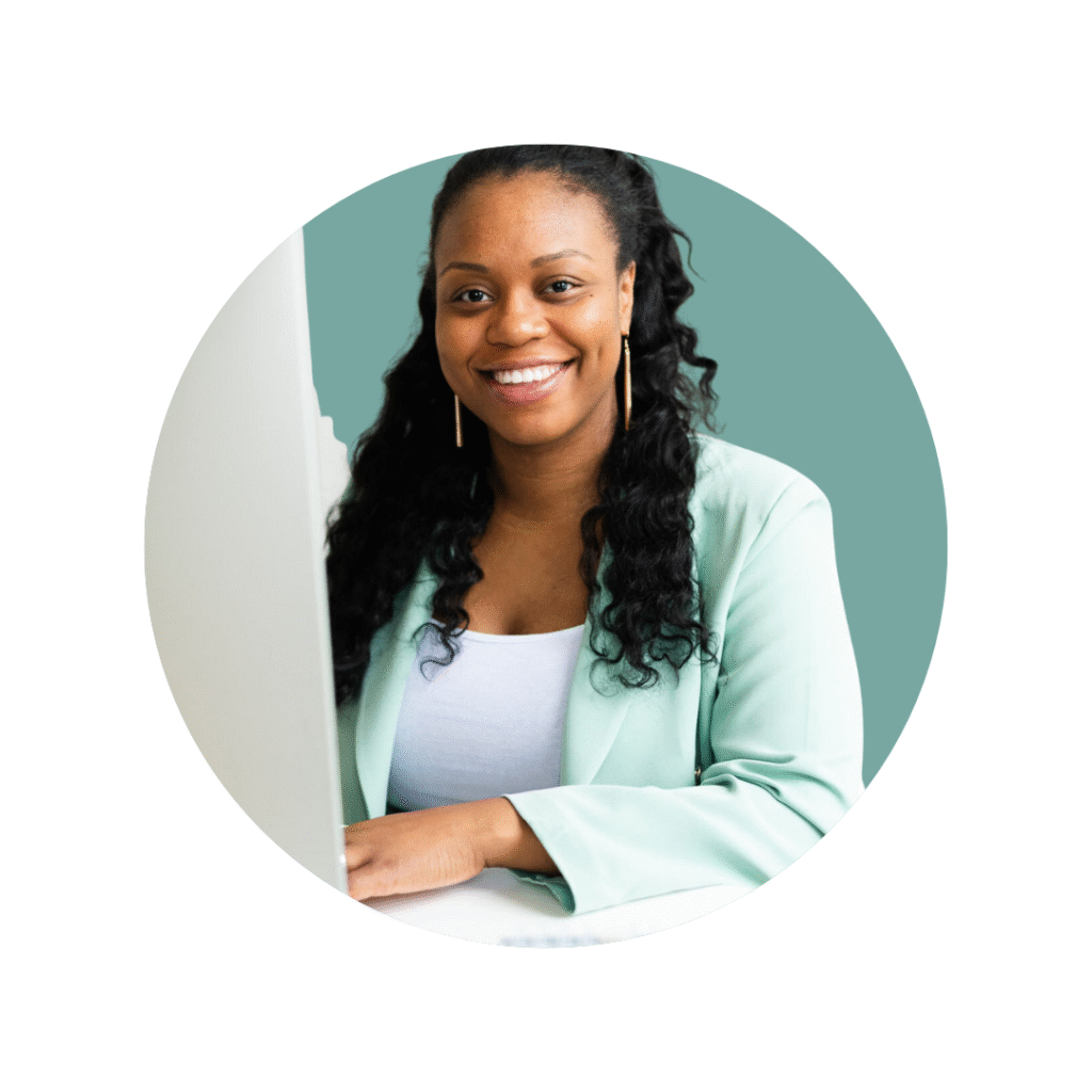 Woman at computer with long dark hair and long earrings in white top and suit jacket smiling at camera