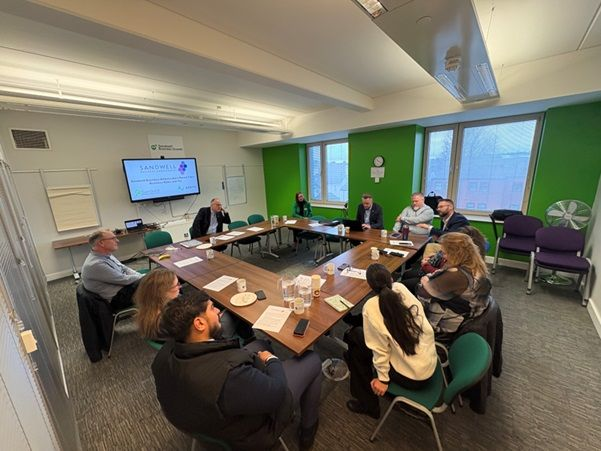 A group of people are sat around a square of tables in discussion 