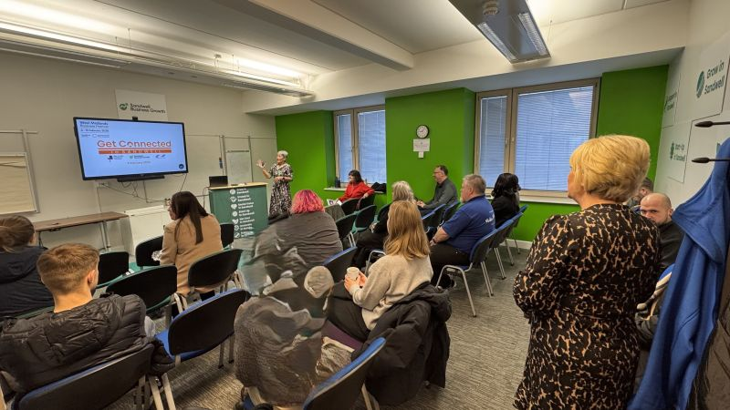 Group of people sat in rows watching a presentation from a woman at the front