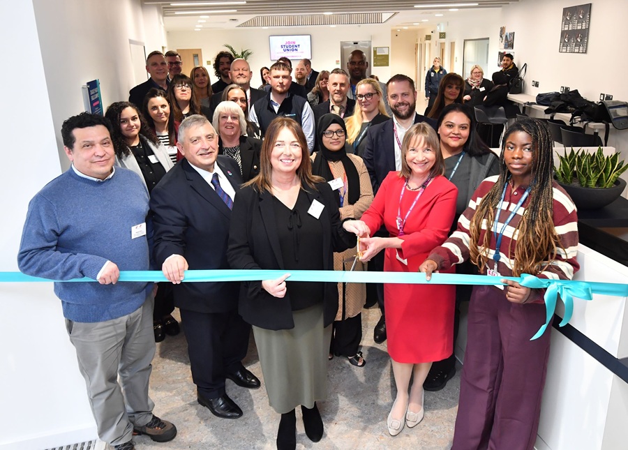 A group of people stand in front of a blue ribbon about to be cut to open the facility