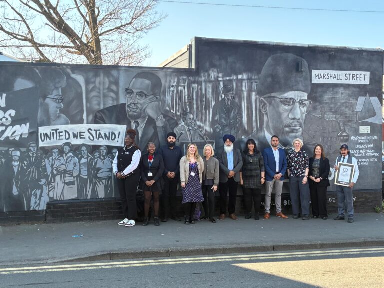 a group of people stand in front of a large Malcolm X piece of street art
