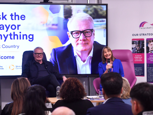 Image of Richard Parker and Lisa Capper sat on chairs in front of an audience with a large screen with Richards face on behind them.